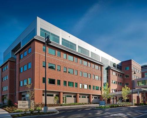 Exterior photo of the entrance at Northwest Specialty Center. Five level, red brick structure against bright blue skies. Newly installed landscaping surrounds facility.