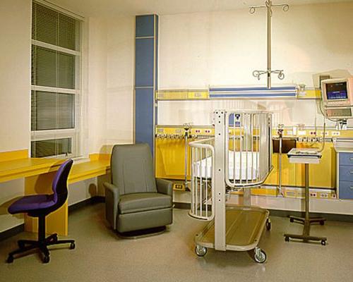 Interior photo of hospital room. Crib bed and chair sit in the middle of the room.